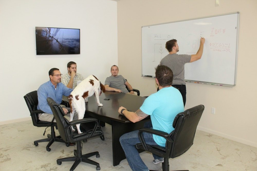 5 Men at a conference table looking at a whiteboard.
