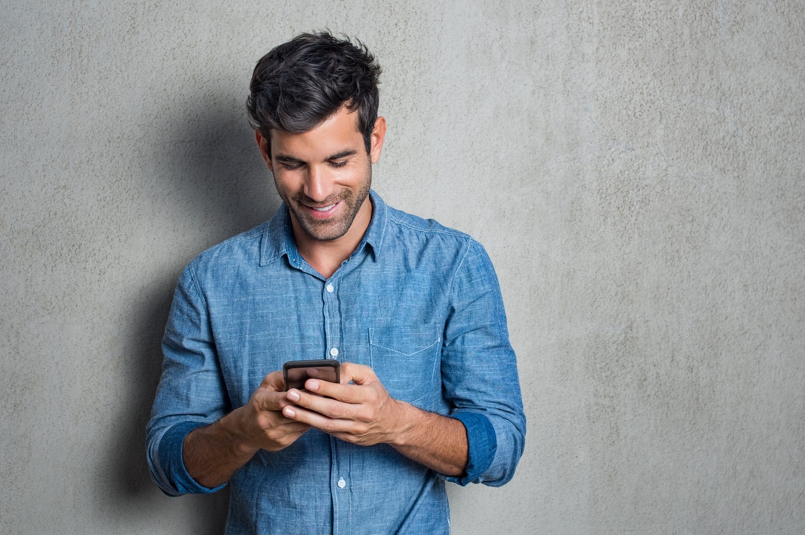 Young man texting message on smart phone isolated on grey background. Using Apps on the phone.
