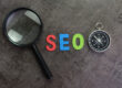 Magnifier glass, colorful alphabet SEO and compass on dark chalkboard background using as SEO Search engine optimization concept.